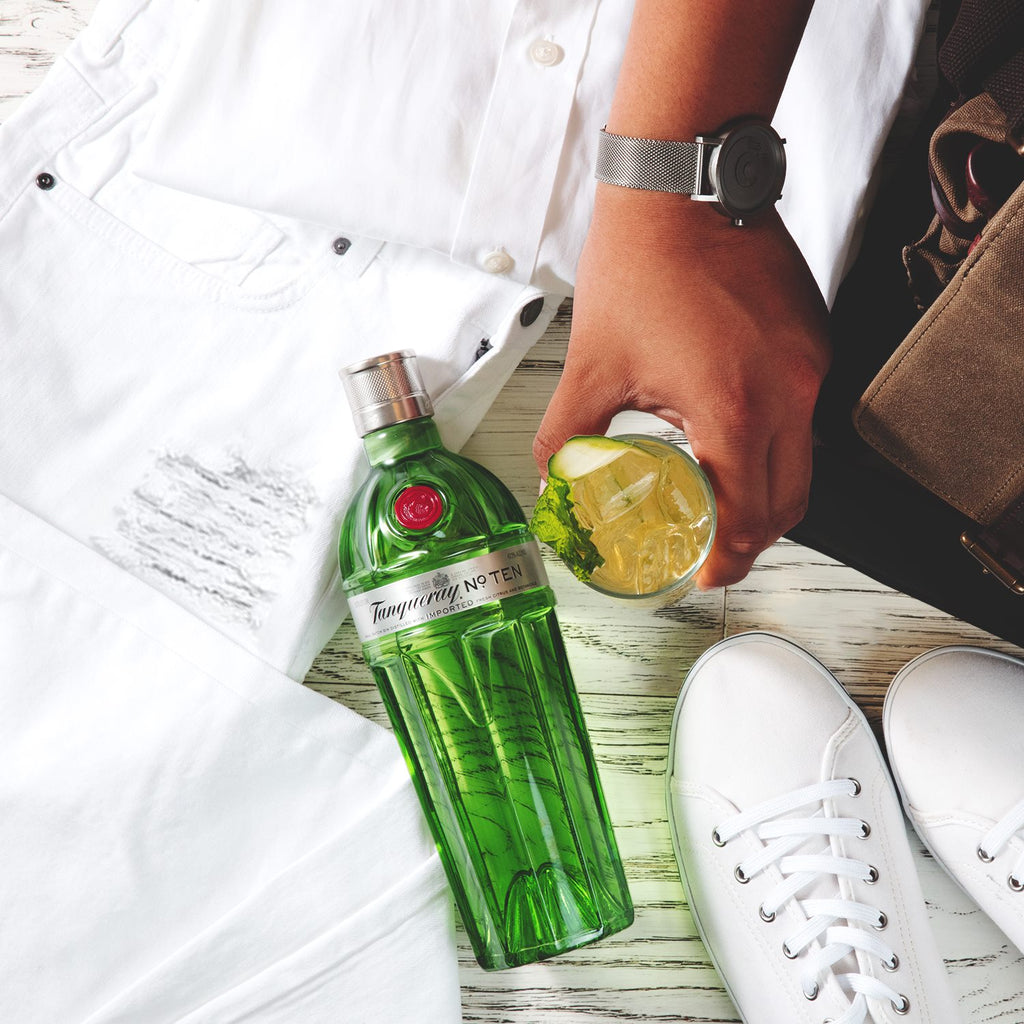 Person holding a bottle of Tanqueray No. Ten gin with a lime wedge on a wooden surface.