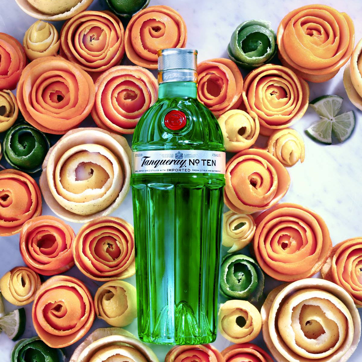 Load image into Gallery viewer, Tanqueray No. Ten gin bottle surrounded by colorful flower-shaped citrus peels on a marble surface