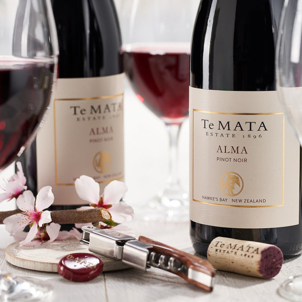 Te Mata Estate Alma Pinot Noir bottles with glasses and a corkscrew on a decorative table.