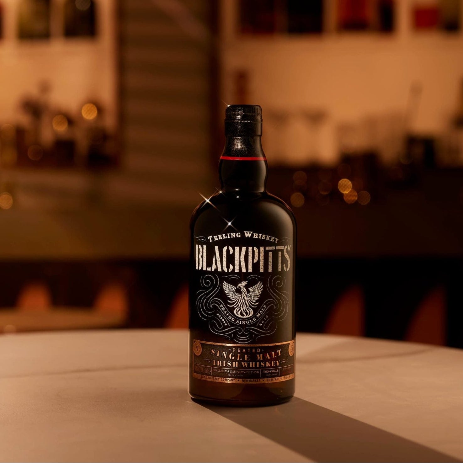 Load image into Gallery viewer, Teeling BlackPitts Irish whiskey bottle on a bar counter with blurred bar background