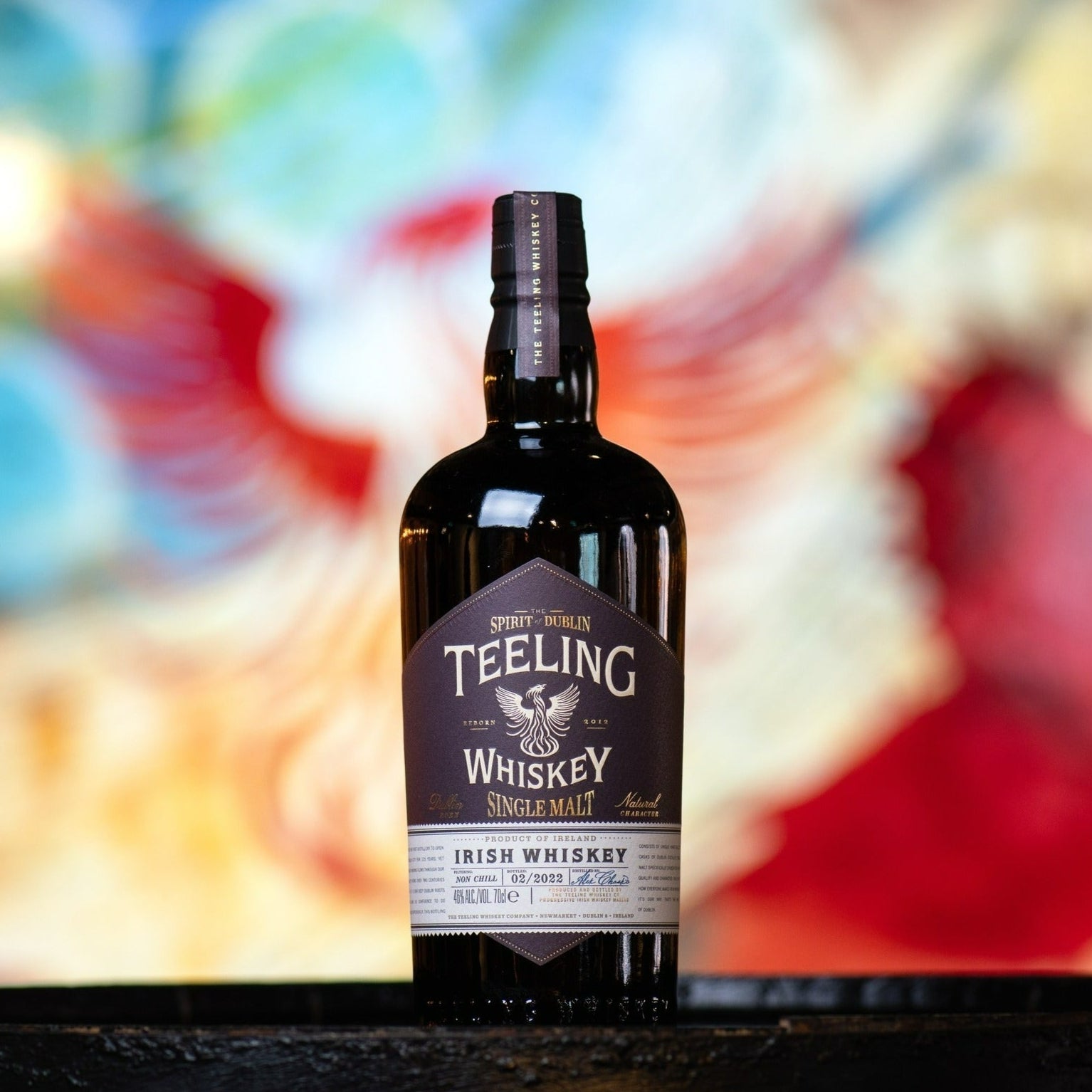 Load image into Gallery viewer, A bottle of Teeling Single Malt Whiskey on a black table with a blurred coloured background