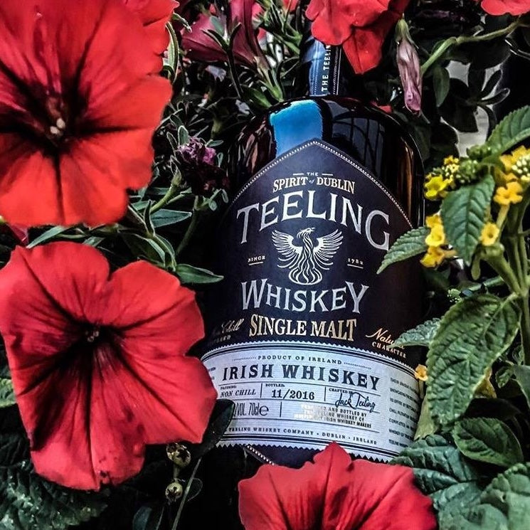 Load image into Gallery viewer, A bottle of Teeling Single Malt Whiskey in the garden with some red beautiful flowers around it