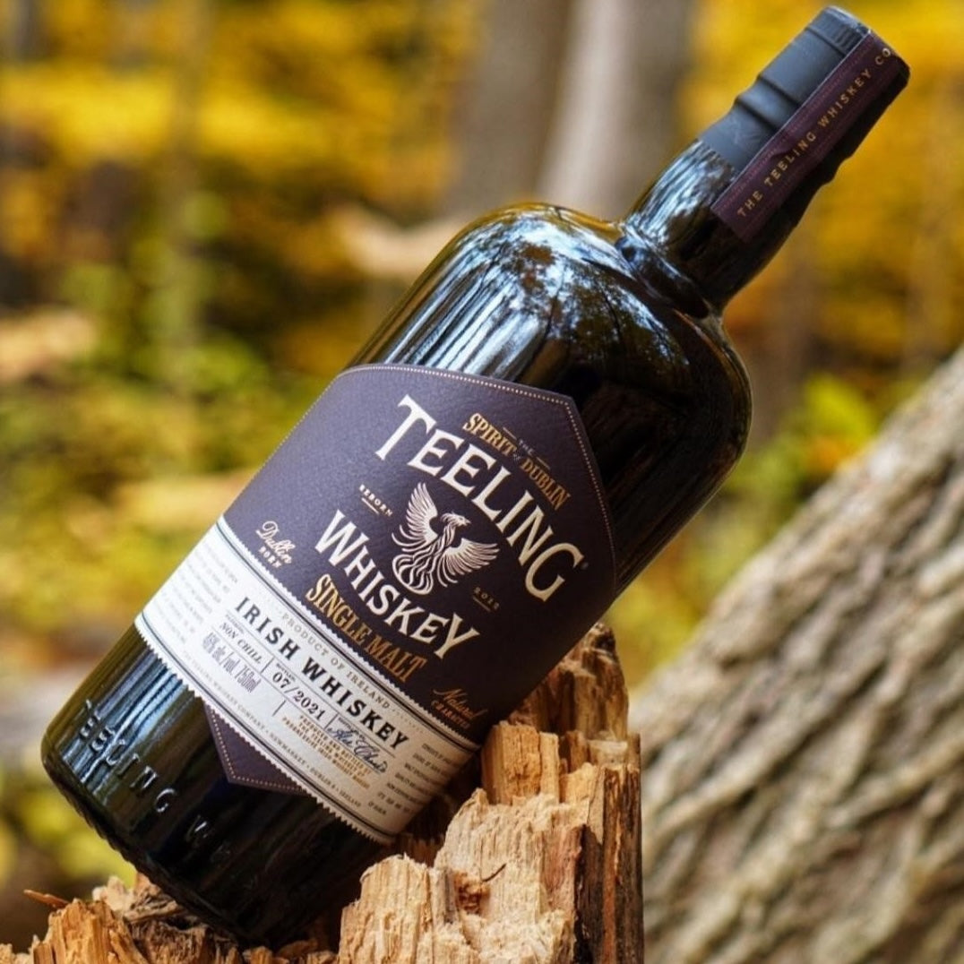 Load image into Gallery viewer, A bottle of Teeling Single Malt Whiskey leaning against som wood in the forest