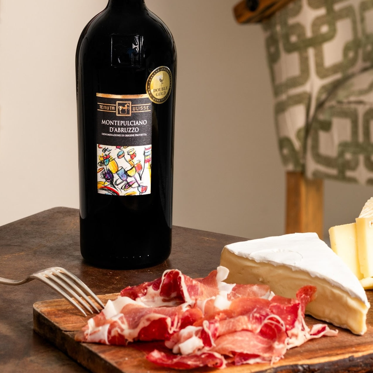 Load image into Gallery viewer, A bottle of Tenuta Ulisse Montepulciano d'Abruzzo next to a cheese wedge and parma ham.