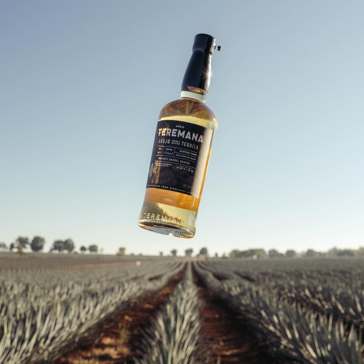 Load image into Gallery viewer, Bottle of Teremana anejo tequila floating in the air above a field with a clear sky.