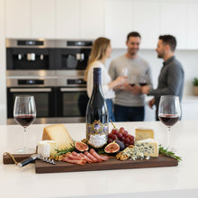 Load image into Gallery viewer, A bottle of Terra-Sancta-Pinot-Noir wine with a charcuterie board on a kitchen counter, with people in the background.