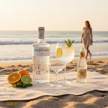 Load image into Gallery viewer, Bottle of The Botanist gin, Fever-Tree Indian tonic water, and a cocktail on a beach with a woman in the background.