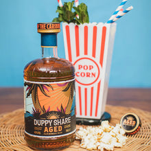 Load image into Gallery viewer, Bottle of Duppy Share Aged rum with popcorn and a popcorn-themed cup on a blue background