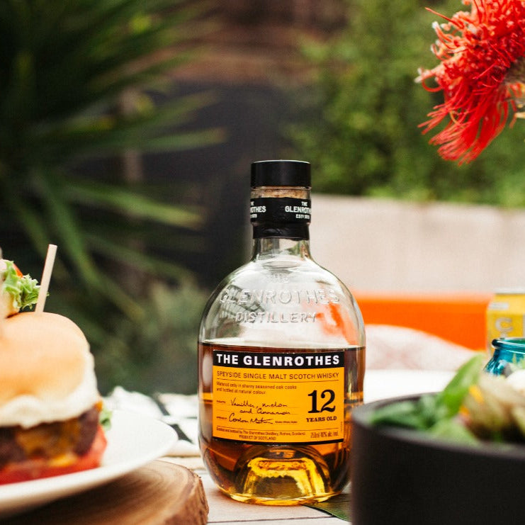 Bottle of The Glenrothes whisky on a table with food and flowers in the background