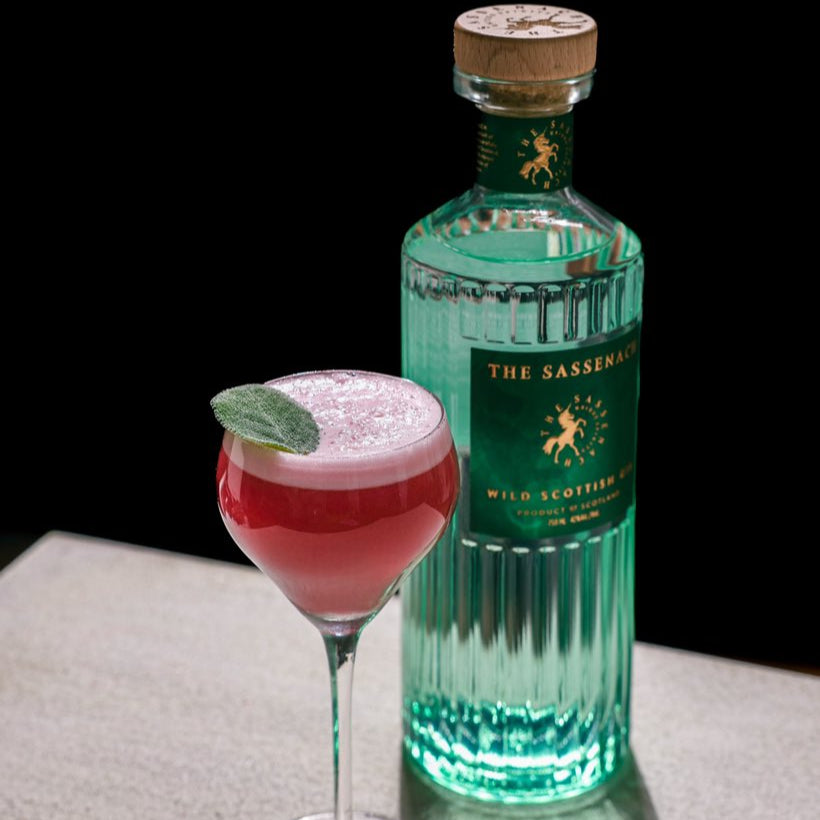 Load image into Gallery viewer, Bottle of 'The Sassenach' gin with a pink cocktail garnished with a leaf on a dark background