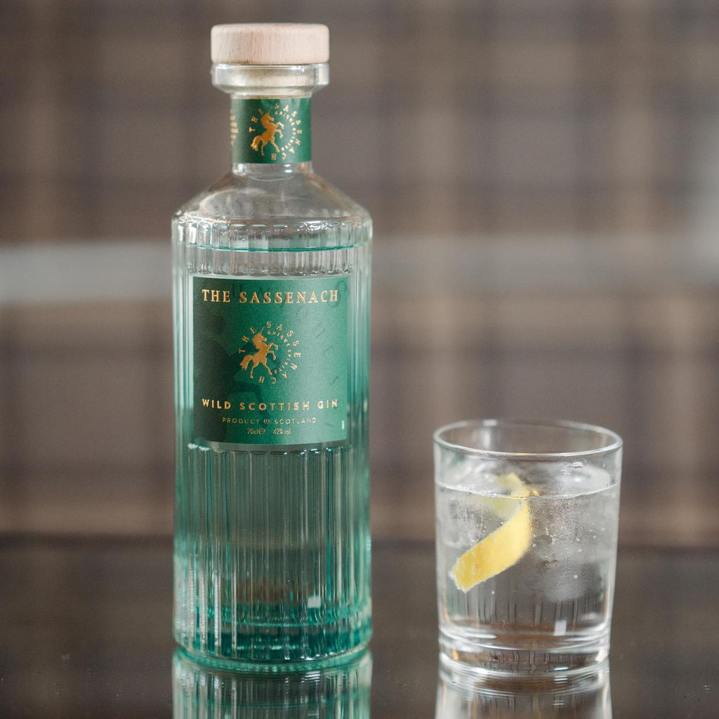 Bottle of The Sassenach gin with a glass of gin and tonic on a reflective surface.
