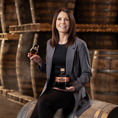 Load image into Gallery viewer, Alex Thomas (master blender) holding a bottle of The Sexton 11 Year Old Single Malt Irish Whiskey and a glass in front of wooden barrels