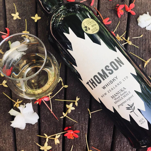 Load image into Gallery viewer, A bottle of Thomson New Zealand Whisky on a table with a tumbler of whisky beside the bottle on a bed of flowers