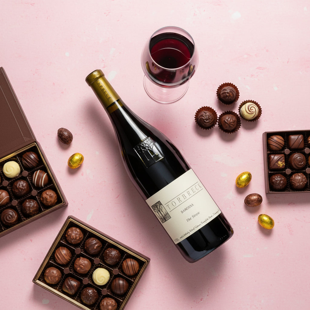 Bottle of Torbreck-Struie-Barossa-Shira wine with a glass and assorted chocolates on a pink background