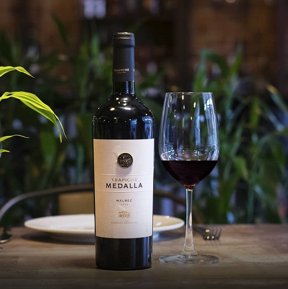 Load image into Gallery viewer, A bottle of close up image of of label next to a half-full glass of red wine on a restaurant table