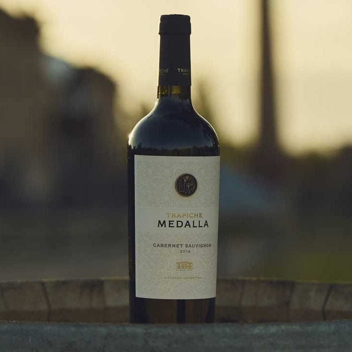 Load image into Gallery viewer, A bottle of Trapiche Medalla Malbec wine on a barrle at sunset