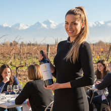 Load image into Gallery viewer, Woman holding a bottle of Trapiche Medalla Malbec wine in a vineyard with other people in the background