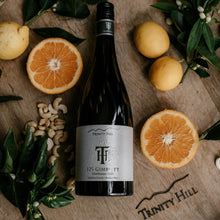 Load image into Gallery viewer, A Trinity Hill 125 Chardonnay wine bottle lying on a wooden barrel with fruits and nuts