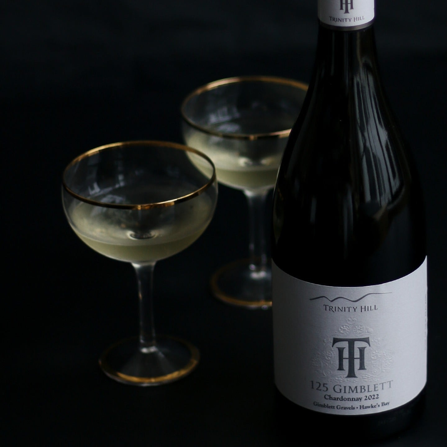 Load image into Gallery viewer, Trinity Hill 125 Chardonnay wine bottle with two glasses on a dark background, featuring a silver medal award on the right.