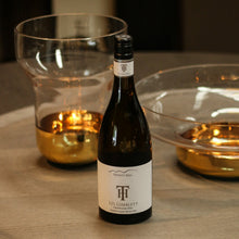 Load image into Gallery viewer, Wine bottle on a wooden table with two glasses in the background