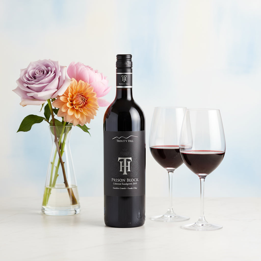 Trinity Hill Prison Block Cabernet Sauvignon wine bottle with two glasses of red wine and flowers on a light background