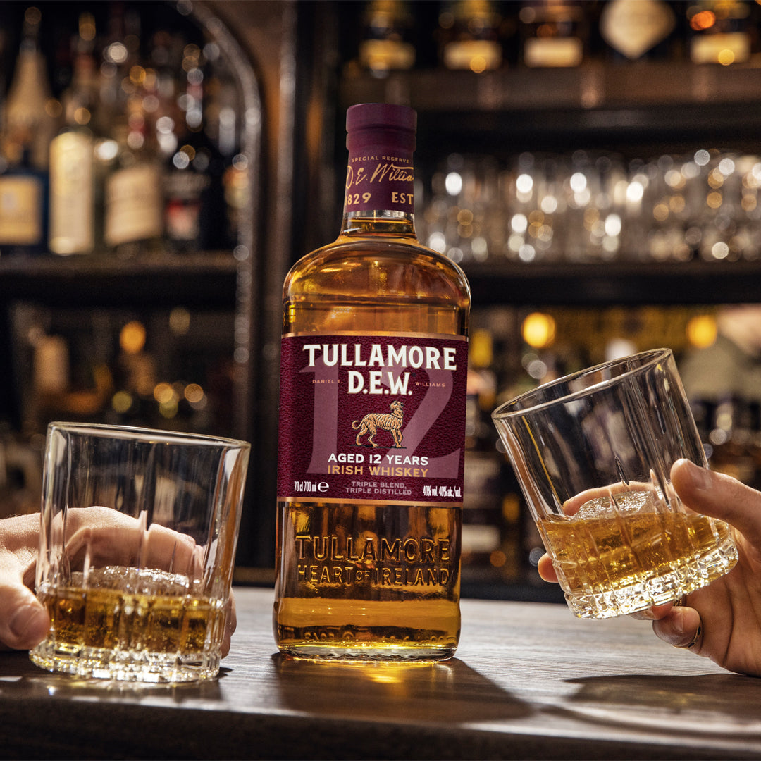 Load image into Gallery viewer, Bottle of Tullamore D.E.W. Irish whiskey with two glasses on a bar.