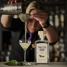 Load image into Gallery viewer, Person pouring a cocktail into a glass with a bottle of &#39;Twelfth Hour&#39; gin on a bar counter.