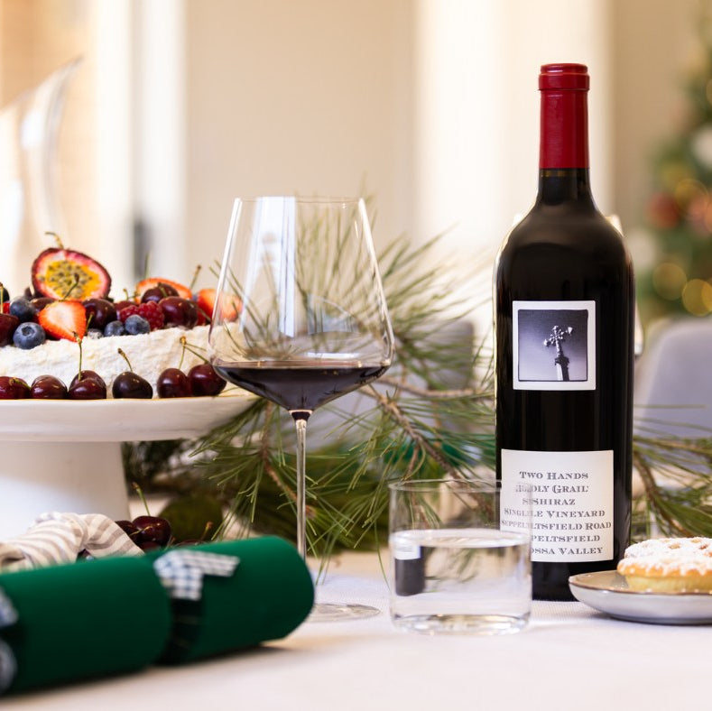 Load image into Gallery viewer, Two Hands Holy Grail Shiraz Seppeltsfield Road red wine bottle, glass, and cake on a festive table with Christmas decorations.