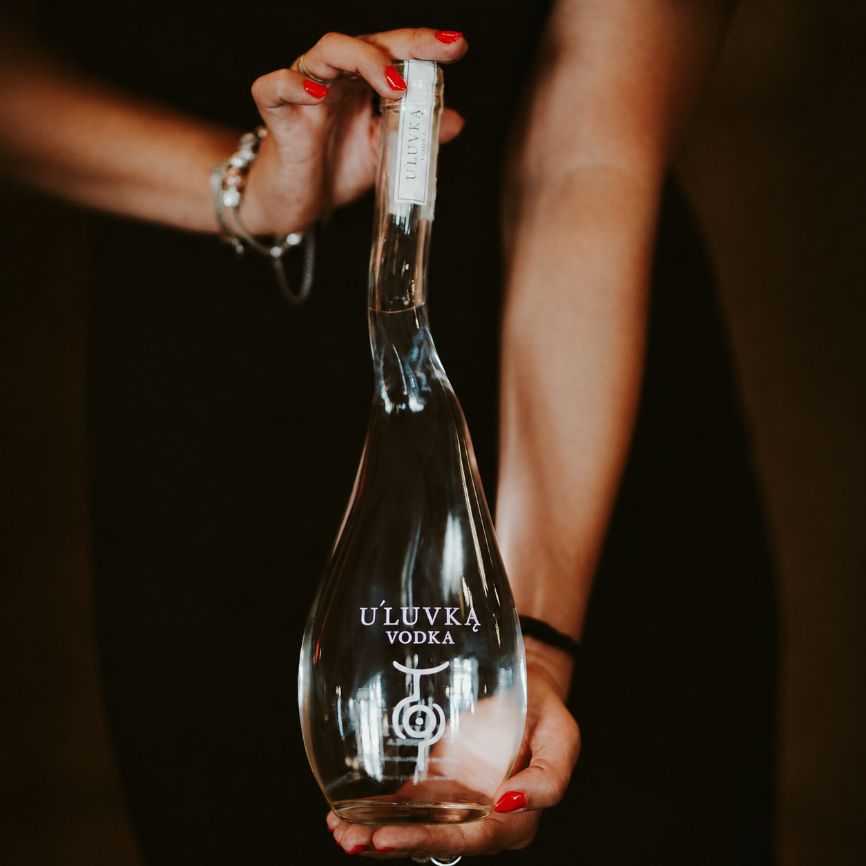 Load image into Gallery viewer, A woman holds a bottle of U'Luvka Vodka against a dark background. The bottle is shaped like a pear and contains crystal clear vodka, with white text and logo printed on the front.