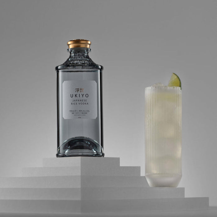 Bottle of gin and a cocktail with a lime wedge on a gray background