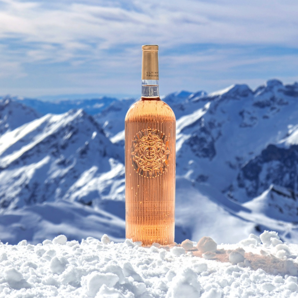 Load image into Gallery viewer, A tall bottle of Ultimate Provence rosé with a gold foil cap and a gold crest on the front, standing upright in a snowy landscape with mountains in the background under a blue sky.