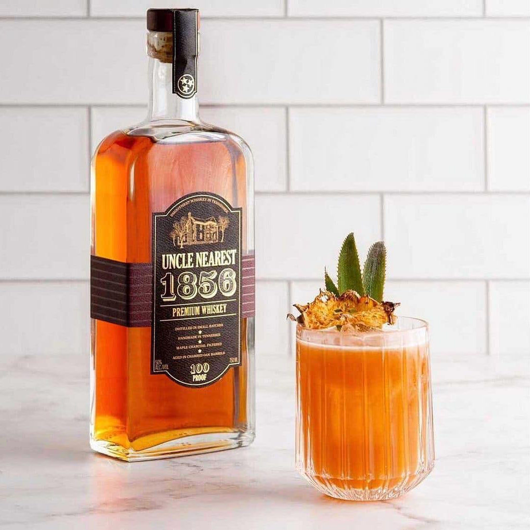 Load image into Gallery viewer, Bottle of whiskey and a cocktail with a pineapple garnish on a marble surface.