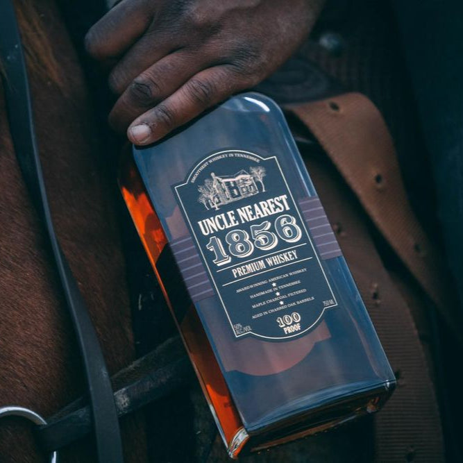 Load image into Gallery viewer, Hand holding a bottle labeled 'Uncle Nearest 1856 Premium Whiskey'.
