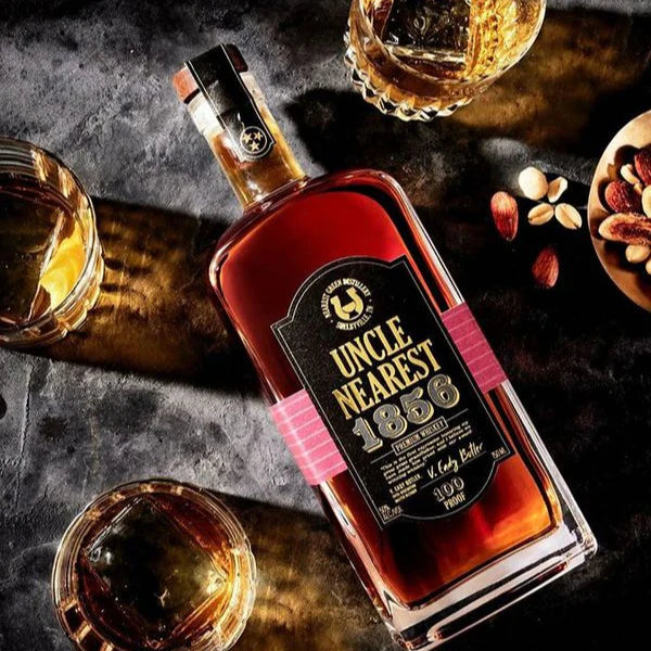Load image into Gallery viewer, A bottle of whisky laying on a table with a few glasses full of whisky on the rocks.