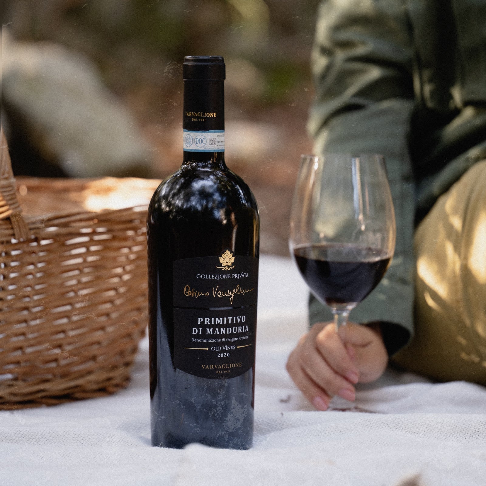 Load image into Gallery viewer, Bottle of Varvaglione Cosimo Collezione Privata Primitivo red wine and glass on a picnic blanket with a blurred background