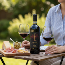 Load image into Gallery viewer, Bottle of Vesevo Ensis Taurasi red wine with two glasses and a charcuterie board on a wooden table outdoors.