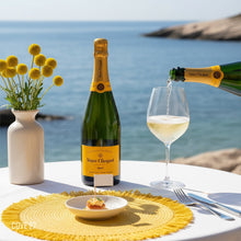 Load image into Gallery viewer, Bottle of Veuve Clicquot champagne being poured into a glass on a table with a scenic ocean view.