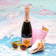 Load image into Gallery viewer, A bottle of Veuve Clicquot Brut Rosé Champagne and a pink bag, sunglasses and a big shell on a blurry backround