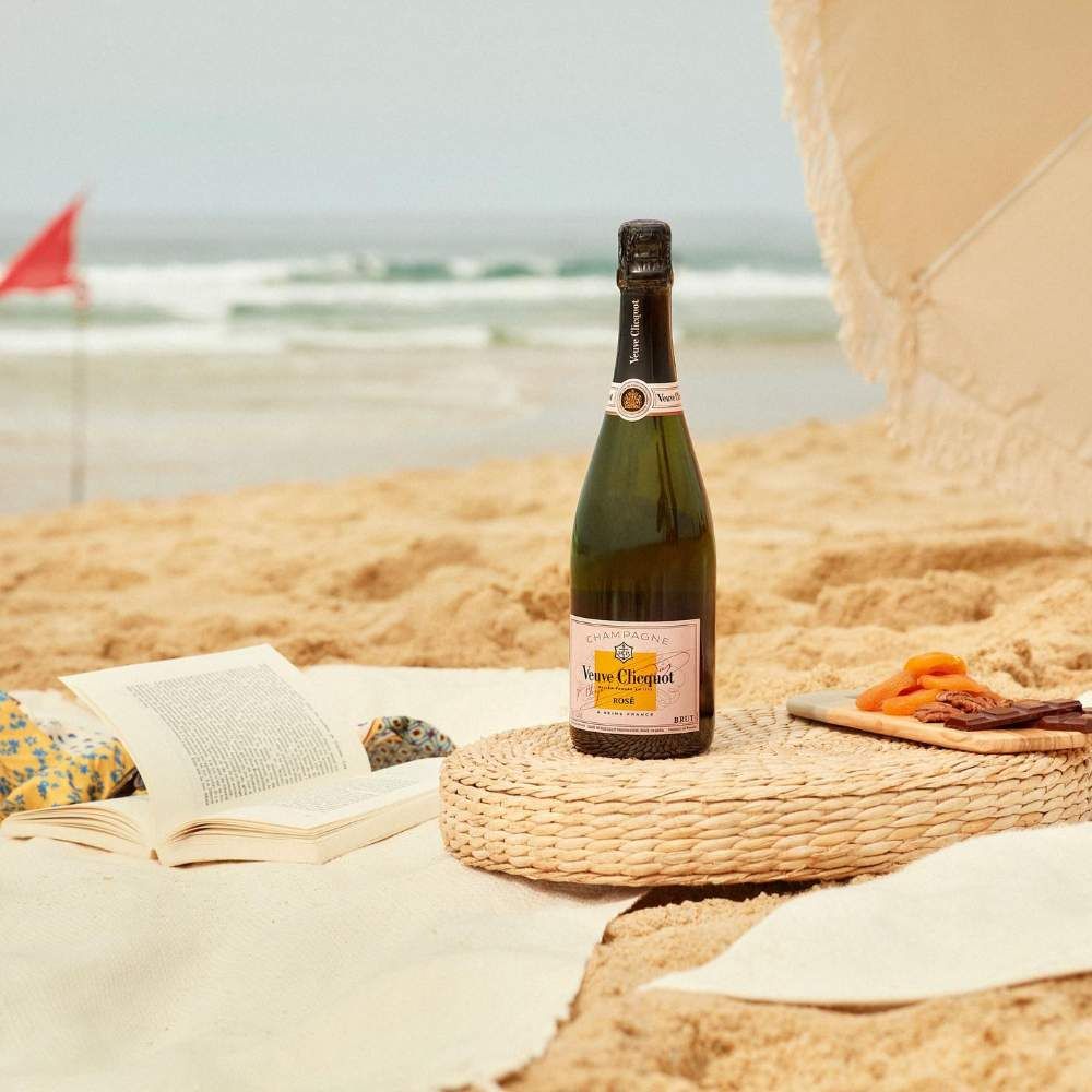 Load image into Gallery viewer, Bottle of Veuve Clicquot rosé champagne on a woven mat with a beach setting in the background