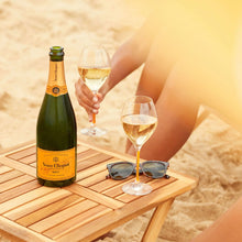 Load image into Gallery viewer, Veuve Clicquot champagne bottle and glasses on a wooden table with a beach background