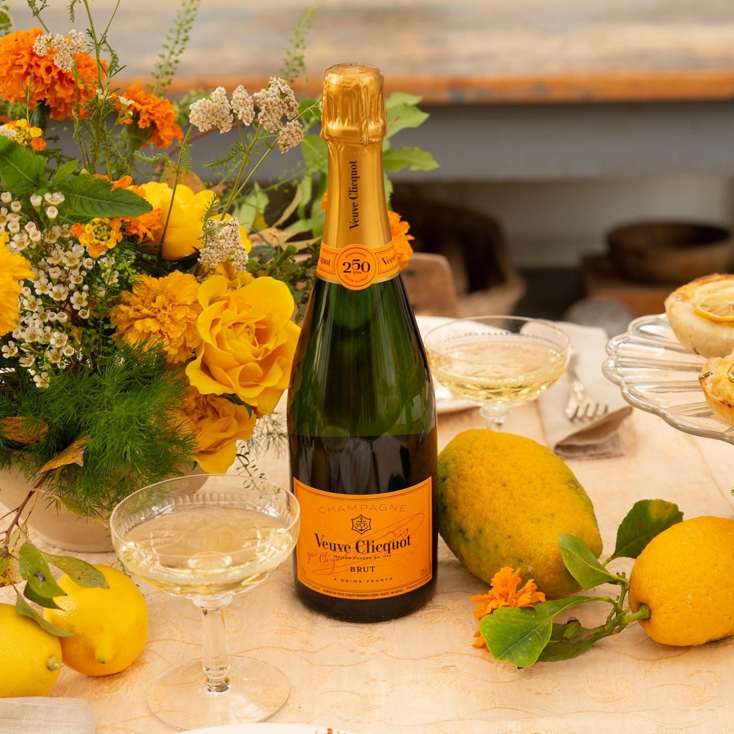 Load image into Gallery viewer, A bottle of Veuve Clicquot Brut Champagne on a table with yellow flowers and lemons on the table