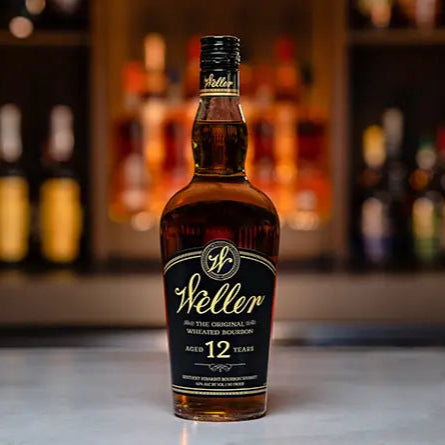 Weller whiskey standing on a white table with lots of bottles on a wall in the background 