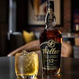Weller Whiskey and a tumbler with whiskey and some ice in it standing on a black table in a livingroom
