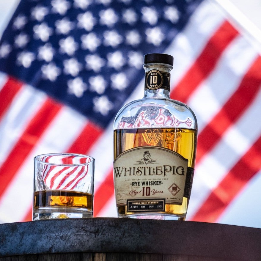 WhistlePig Rye Whiskey bottle with a glass in front of an American flag background