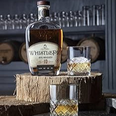 WhistlePig Small Batch Rye bottle standing on a piece of wood with a glass of whiskey and ice