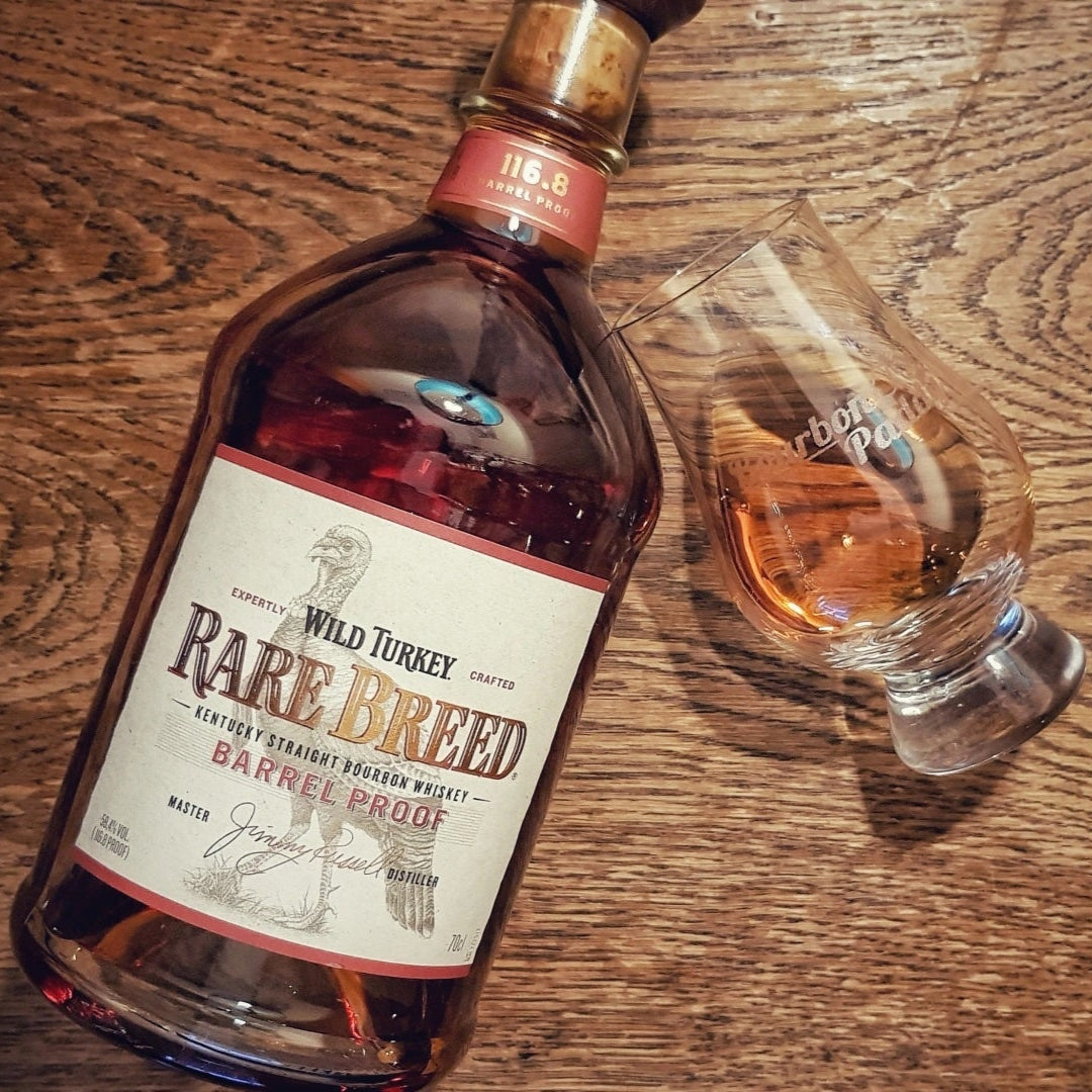 Load image into Gallery viewer, Bottle of Wild Turkey Rare Breed bourbon on a wooden surface with a glass filled with whiskey.