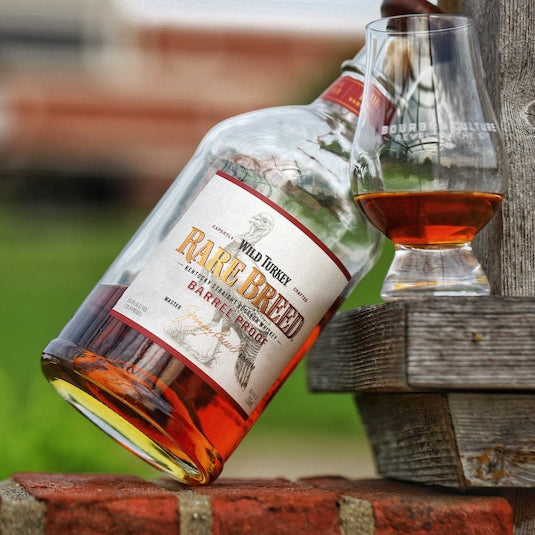 Load image into Gallery viewer, Wild Turkey Rare Breed whiskey bottle and glass on a wooden surface with blurred background