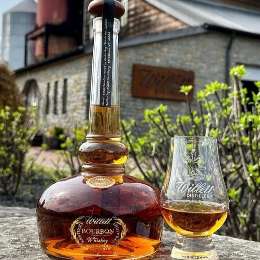 Load image into Gallery viewer, A bottle of Willett Pot Still Reserve Bourbon Whiskey standing on a wall made of stone in front of the distillery