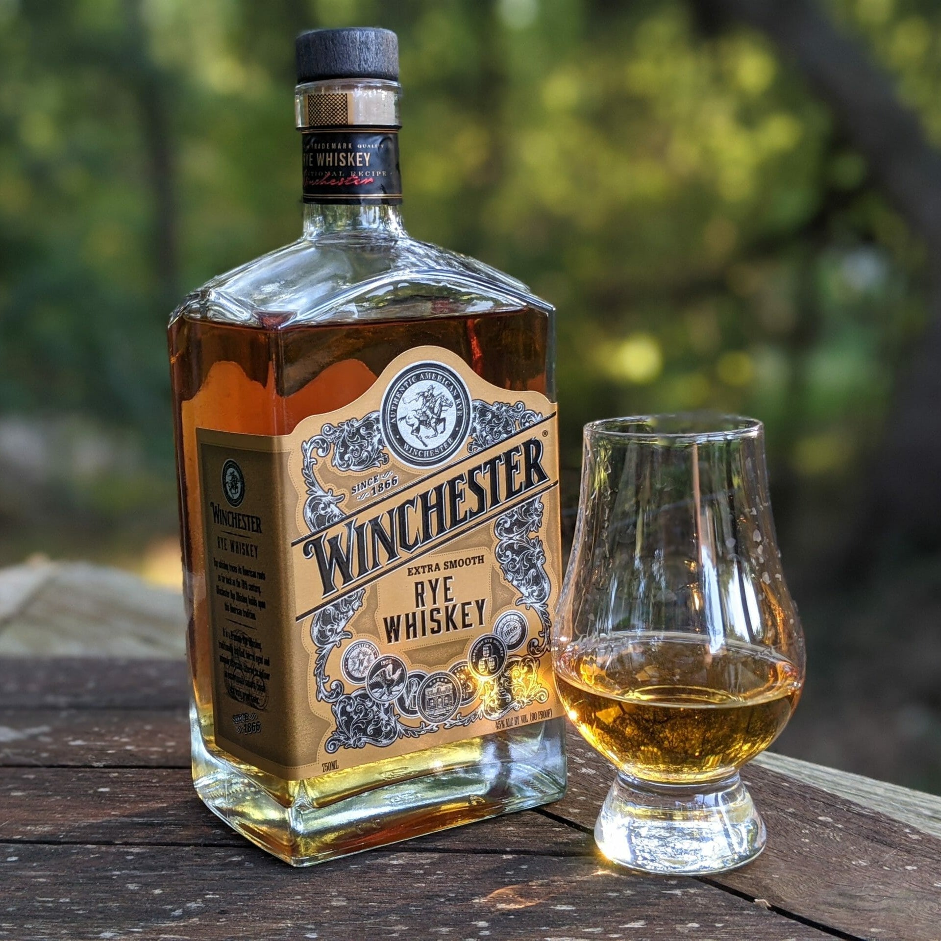 Load image into Gallery viewer, Bottle of Winchester Rye Whiskey with a glass on a wooden surface outdoors.