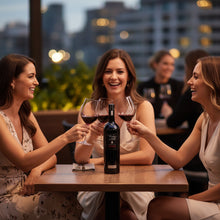 Load image into Gallery viewer, Three women enjoying Wirra Wirra Vintage Bell Cabernet Sauvignon wine together at a rooftop bar with cityscape in the background